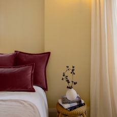 A bedroom painted in Lick's Yellow 07 with voile curtains and dark red pillows on the bed