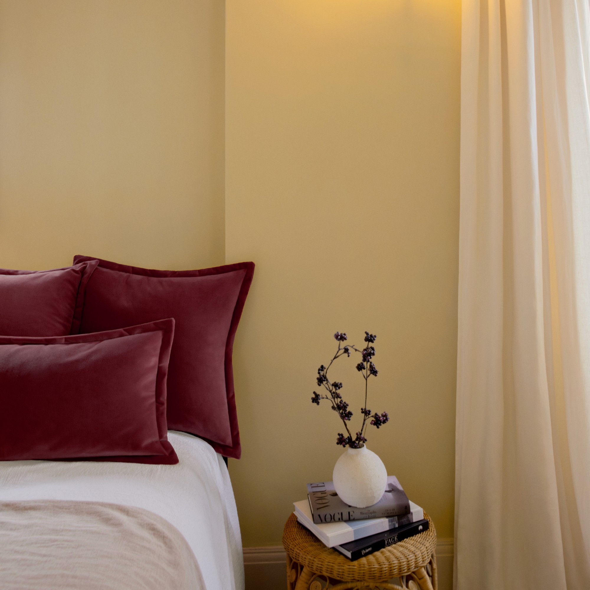 A bedroom painted in Lick&#039;s Yellow 07 with voile curtains and dark red pillows on the bed