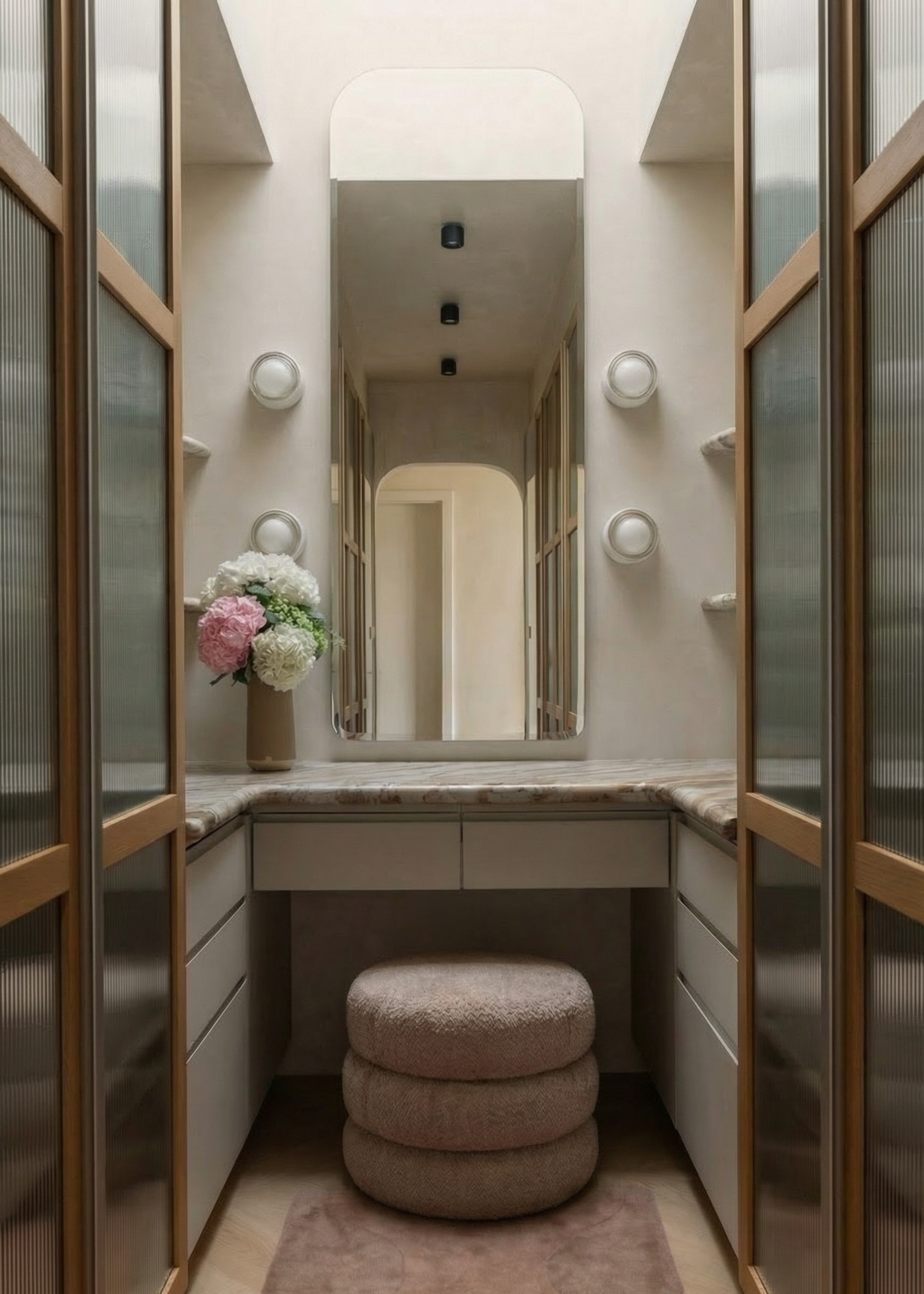A vanity with off-white walls, a curved wall mirror, wall light sconces, a stone counter, and a stacked stool