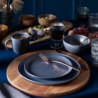 Dark blue table with wooden placemat and two stacked grey plates