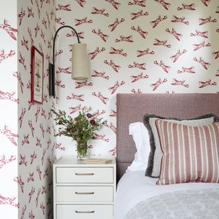Bedroom with patterned wallpaper and curved, shaded wall light beside bed