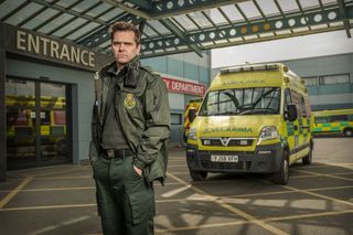 A posed shot of Michael Stevenson outside Holby ED with an ambulance in the background.