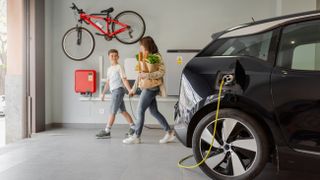 A car charging in a garage while a mother and son leave with a bicycle on the wall