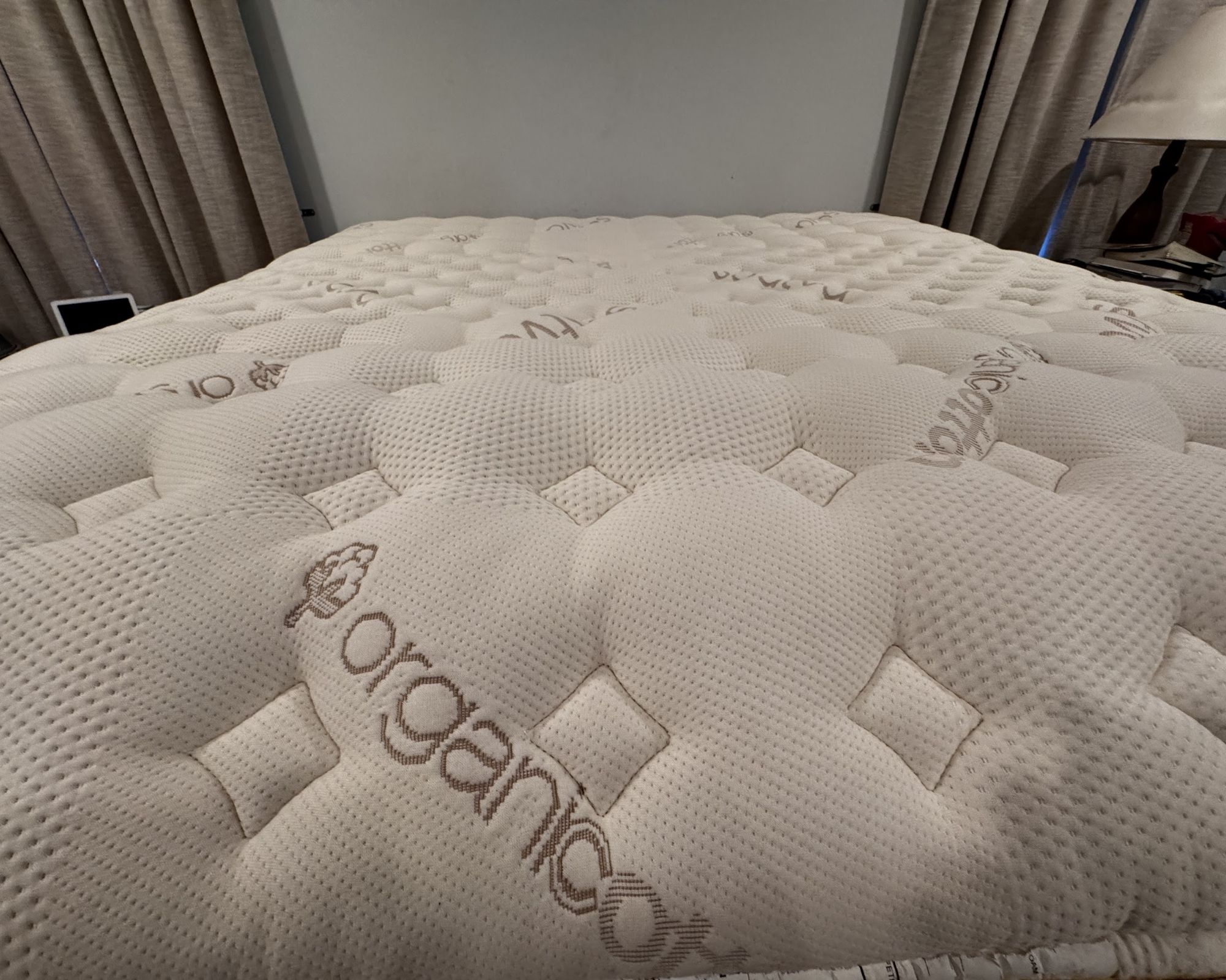 The surface of the Saatva RX Mattress shown with a pale blue wall and tan curtains behind.