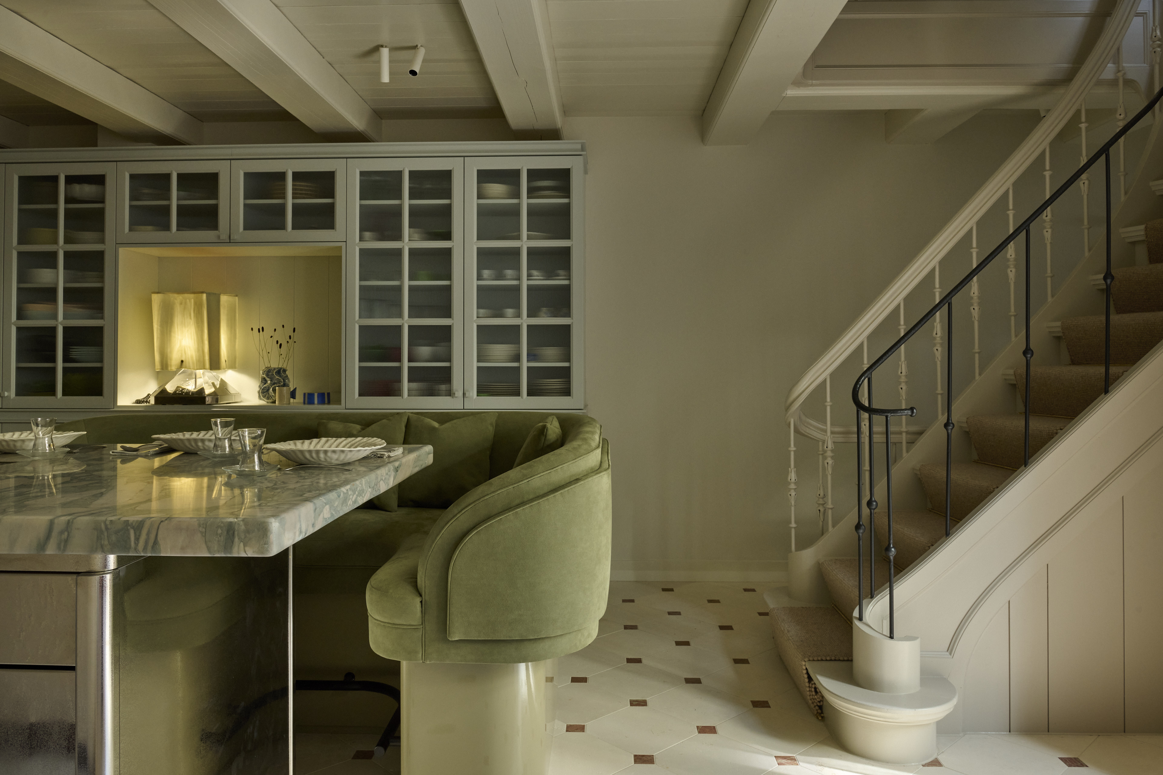 a sage green bench around a marble kitchen island in a kitchen with stairs leading off out of frame