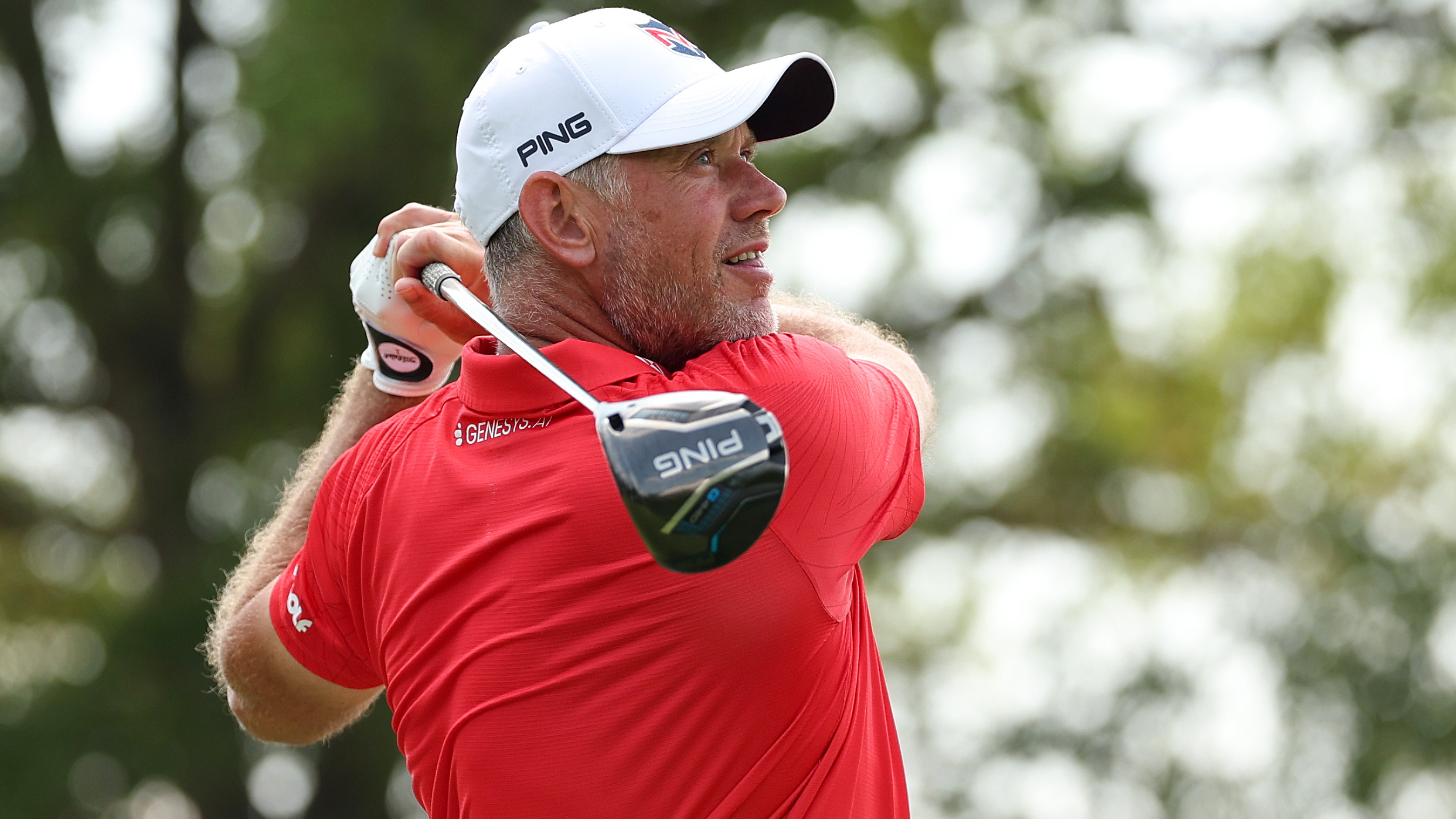 Lee Westwood, wearing a red polo and white cap, holds his finish on a drive