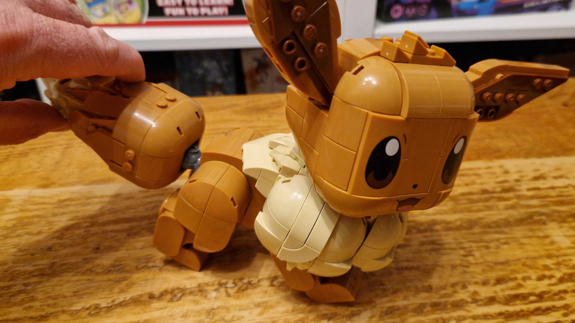 A hand moves the Lego Eevee tail while it stands on a wooden surface