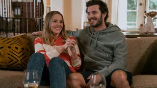 Kristen Bell holding her hands together and Adam Brody puttin his arm behind her on a couch. They're both smiling in Nobody Wants This.