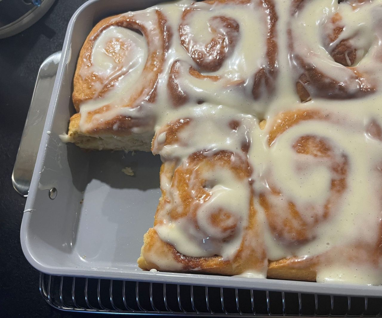 Iced cinnamon rolls in a grey baking tin, with one corner piece removed