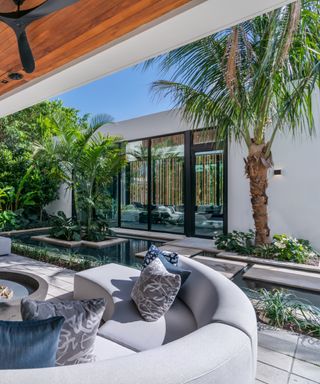 Backyard with curved furniture, water feature, view of interior, awning, tropical trees,