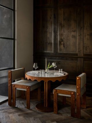 A whimsically designed table sits in a brutalist corner of a French restaurant drenched in wood tones.