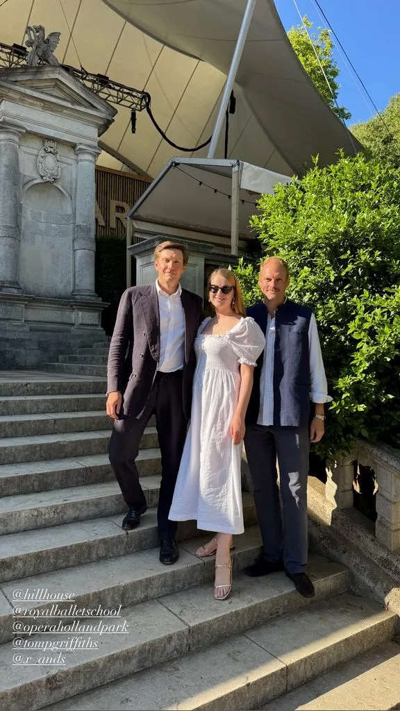 Flora Vesterberg posing on a staircase at the royal ballet school in a white dress with two men