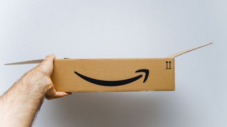 A person holds an open Amazon Prime box up in front of a white wall.