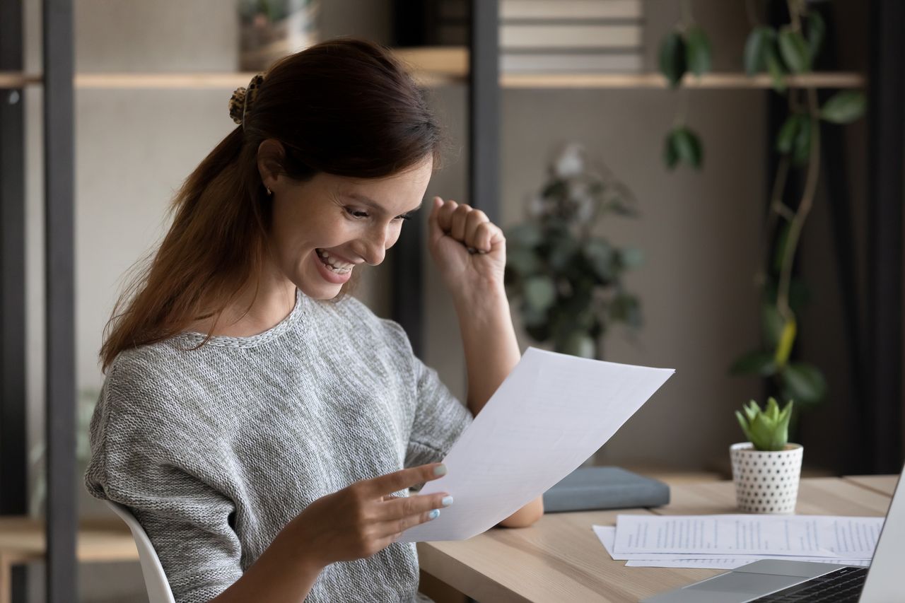 A woman looks delighted and surprised as she reads a document, ostensibly about her inheritance.