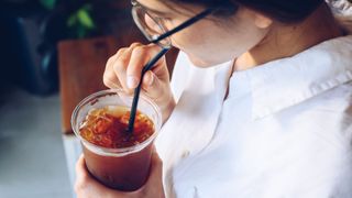 Woman sipping on iced black coffee out of takeaway cup