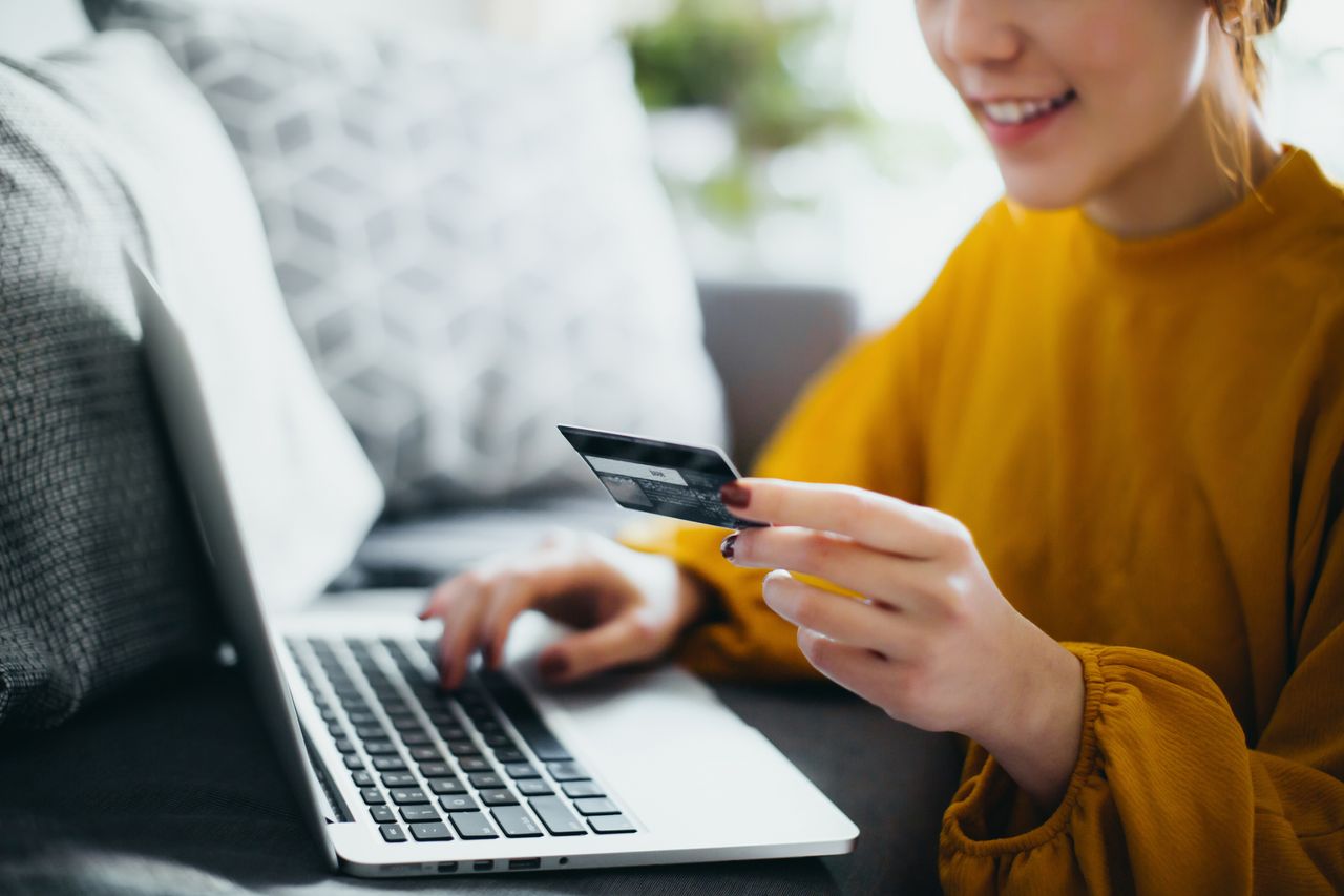 Close up of woman sitting on the floor by the sofa, managing financial bill payment with laptop and credit card on hand at cozy home. Technology makes life so much easier