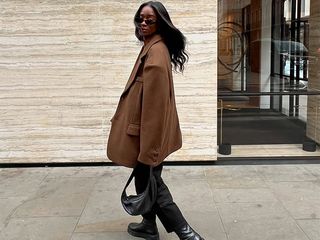 influencer wears brown coat, black pants, and chunky soled boots while carrying a black shoulder bag