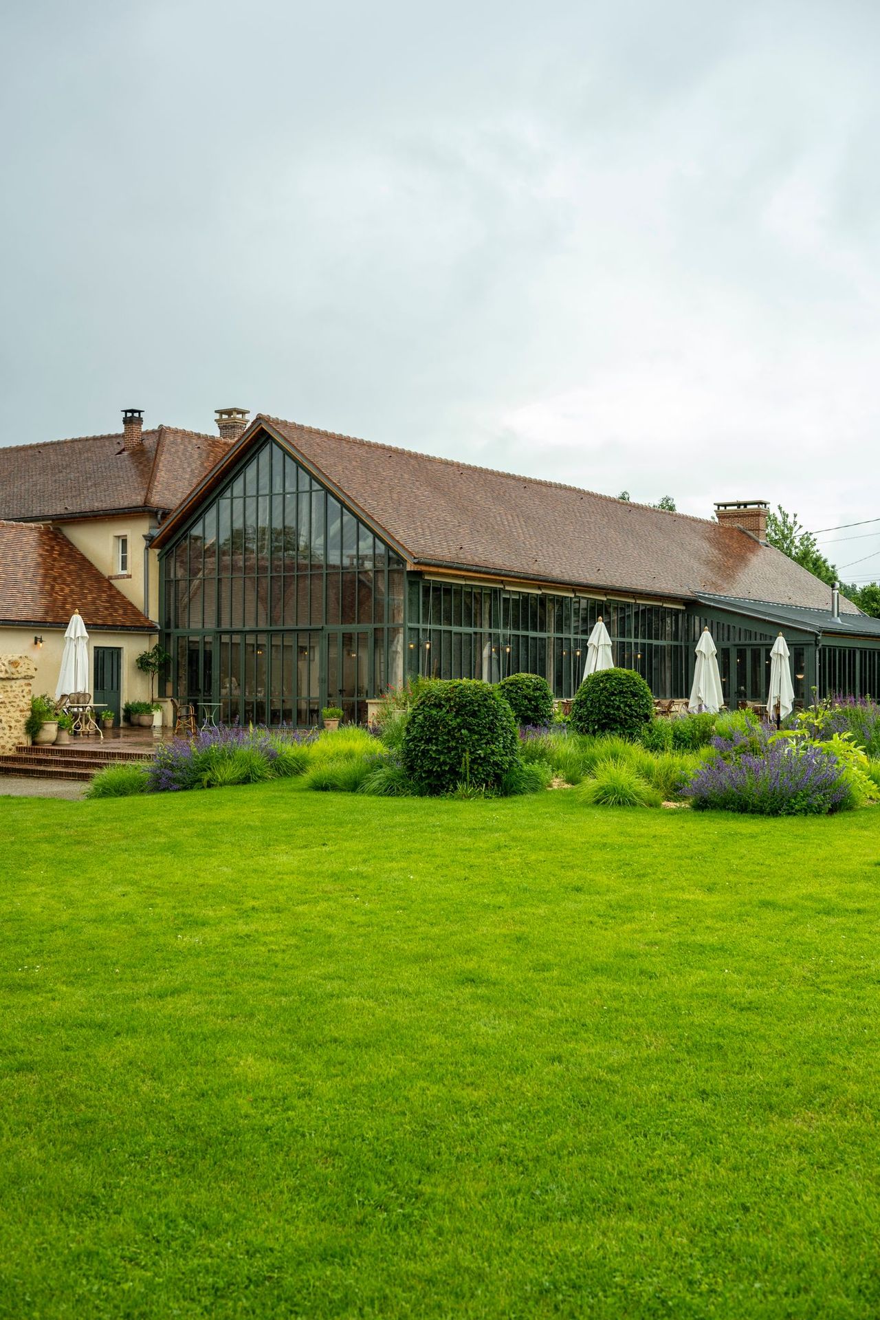 The exterior of a sleek, glass and metal-clad barn conversion is immersed in green.