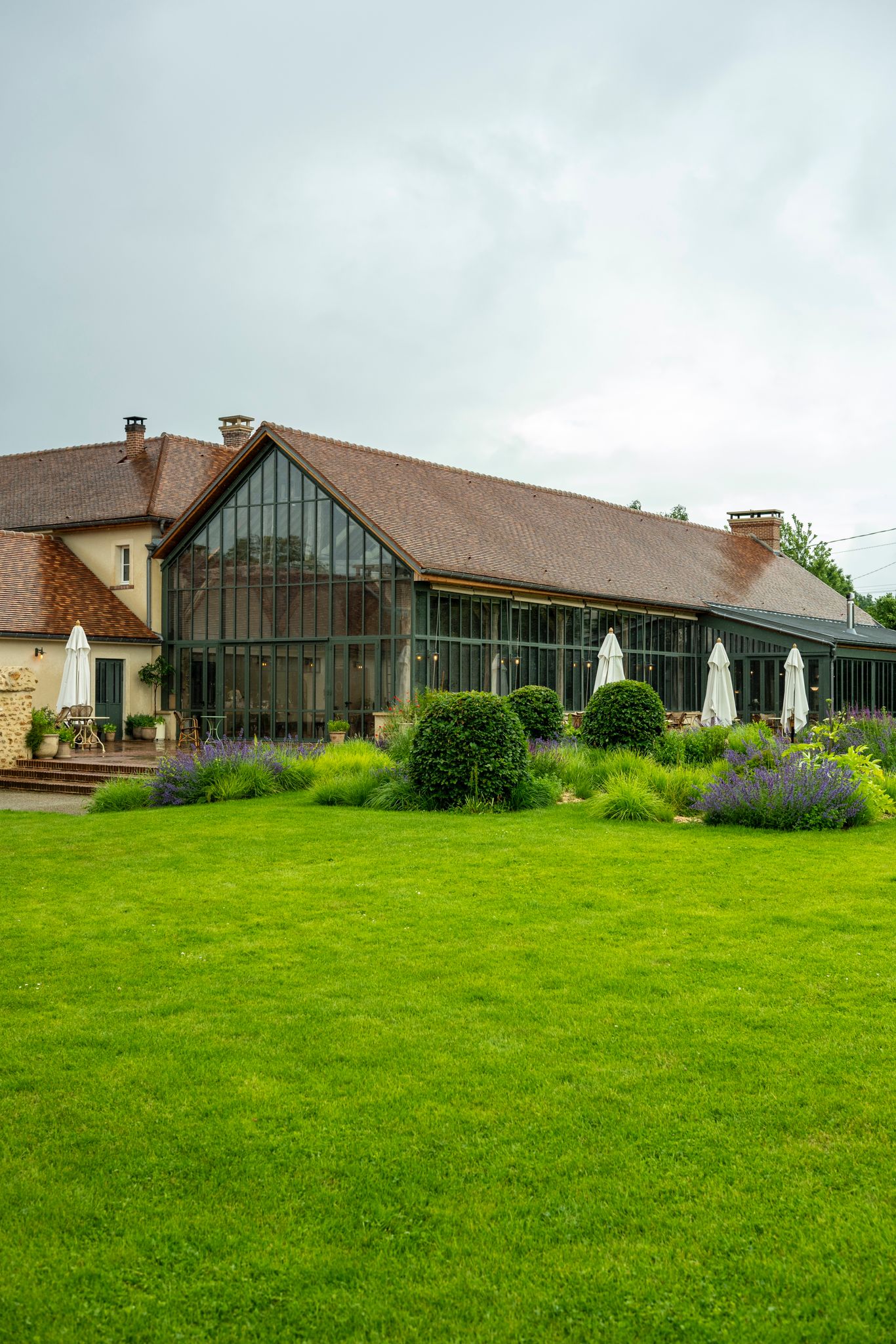 The exterior of a sleek, glass and metal-clad barn conversion is immersed in green.