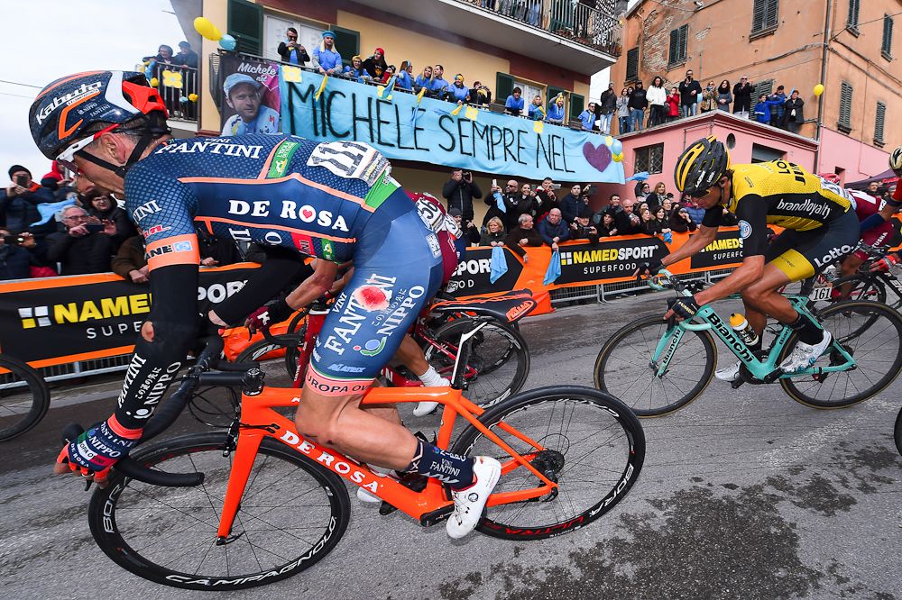 Riders pass a banner honouring Michele Scarponi during stage 5 at Tirreno-Adriatico
