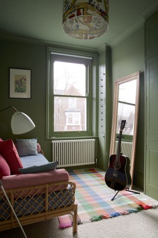 Green guest bedroom with rattan day bed, mirror and guitar