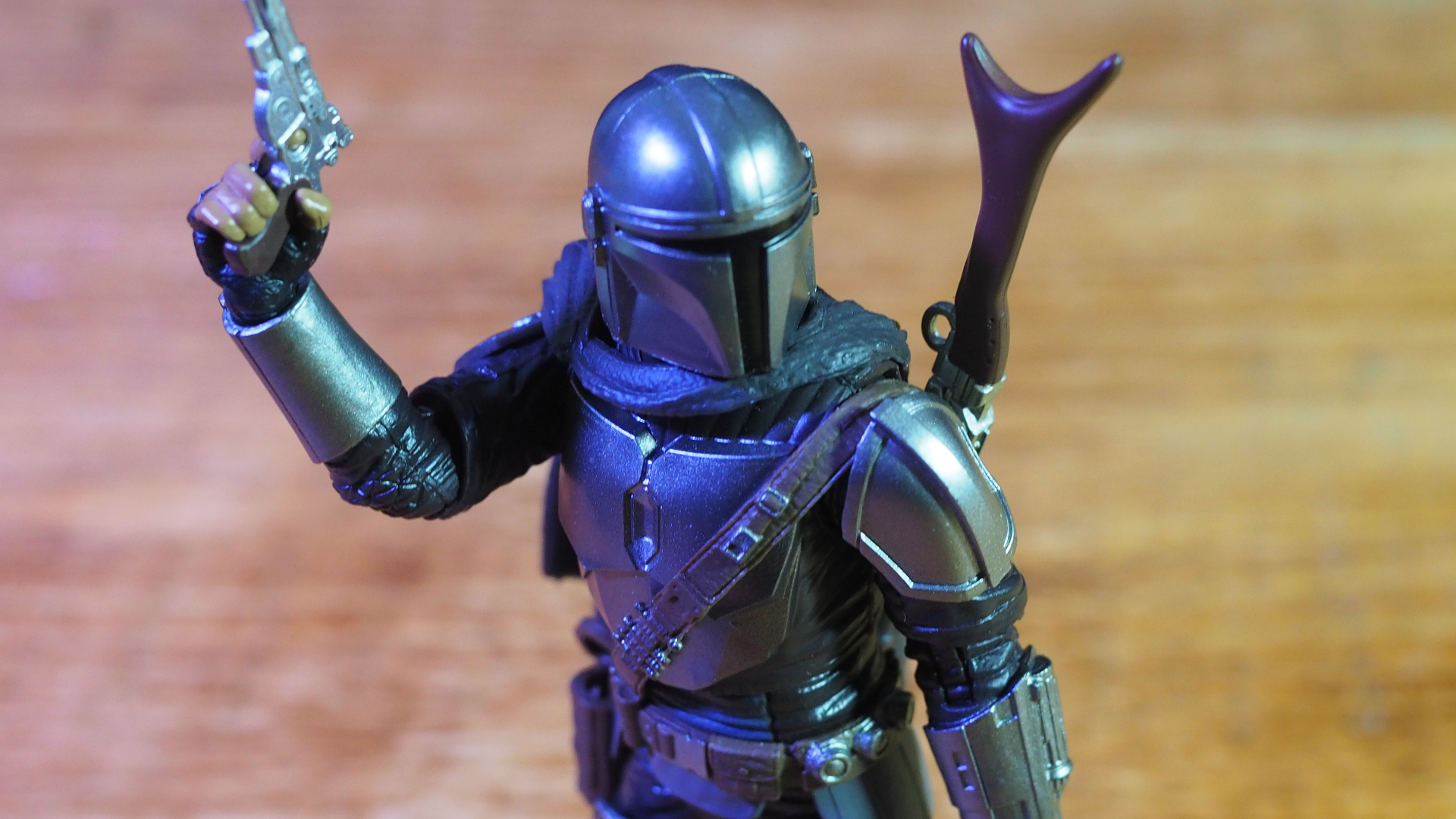 The Mandalorian Black Series action figure holding a blaster and looking off to one side, against a wooden background