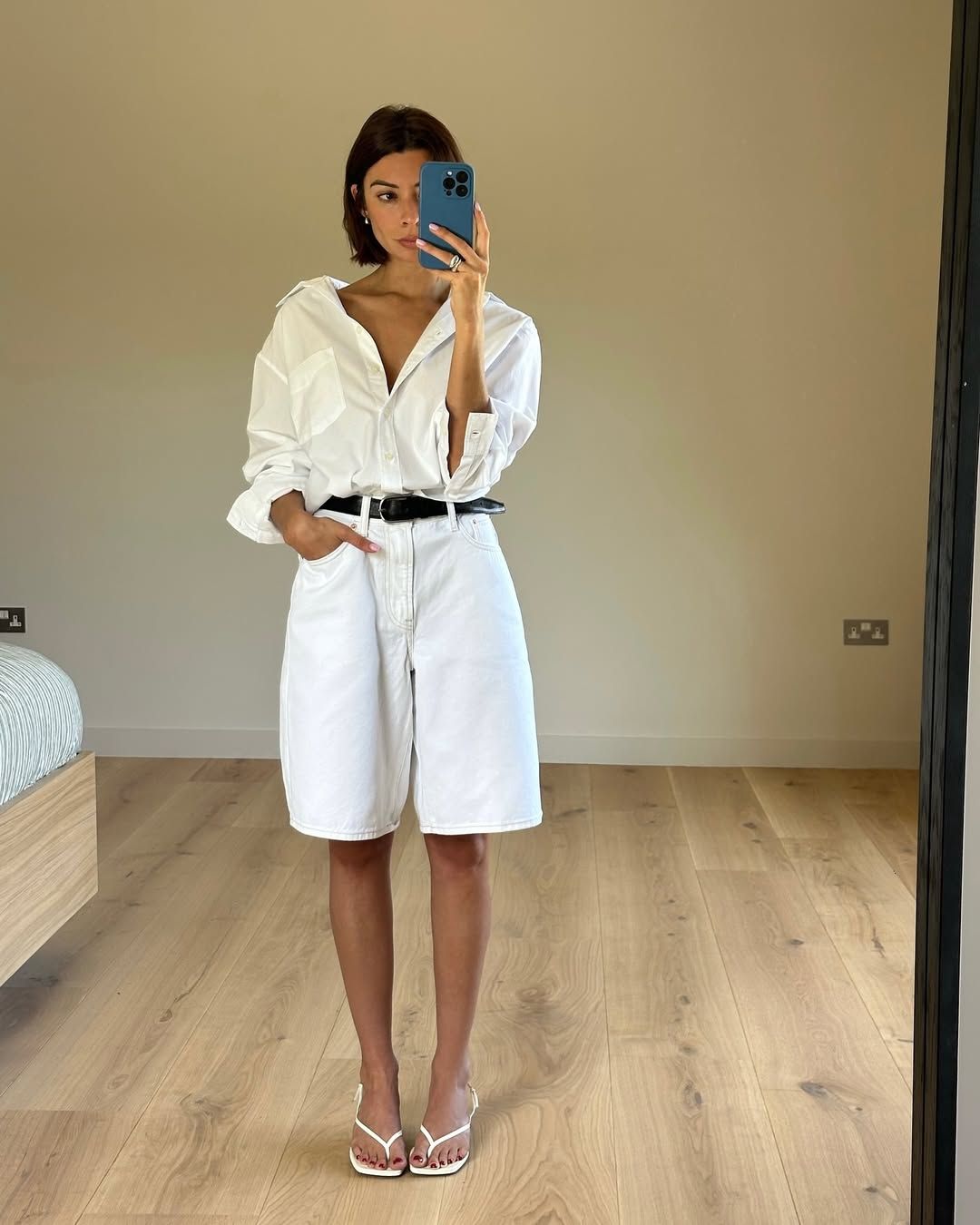 Woman wearing white button-down shirt with white long denim shorts and belt in a summer 2025 outfit.