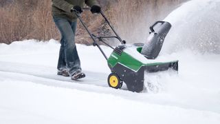 A person using a green snow blower to remove snow