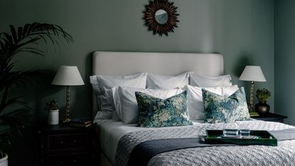 A blue bedroom with a styles bed with white duvet and dark blue throw pillows and blanket