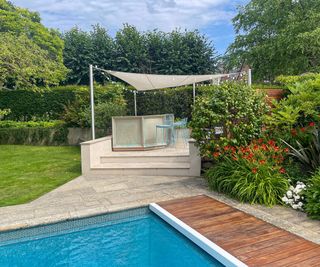 A raised garden bar area with shade sail providing a relaxing outdoor entertaining space next to a swimming pool