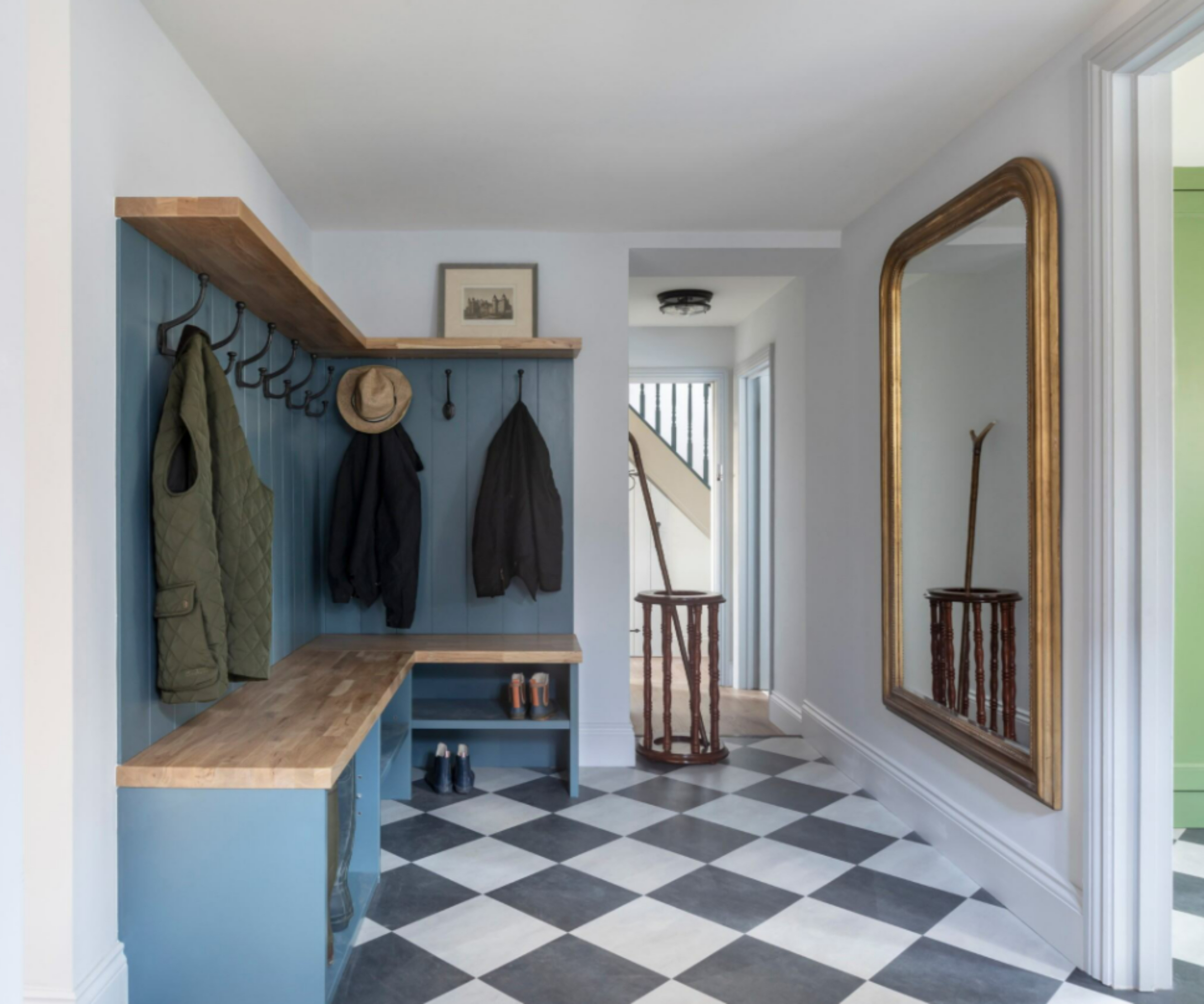 hallway with black and white chequerboard tiles, blue built in storage and seating with panelled wall behind, large gold mirror opposite
