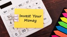 a yellow Post-it note placed on top of a calculator that reads "invest your money"
