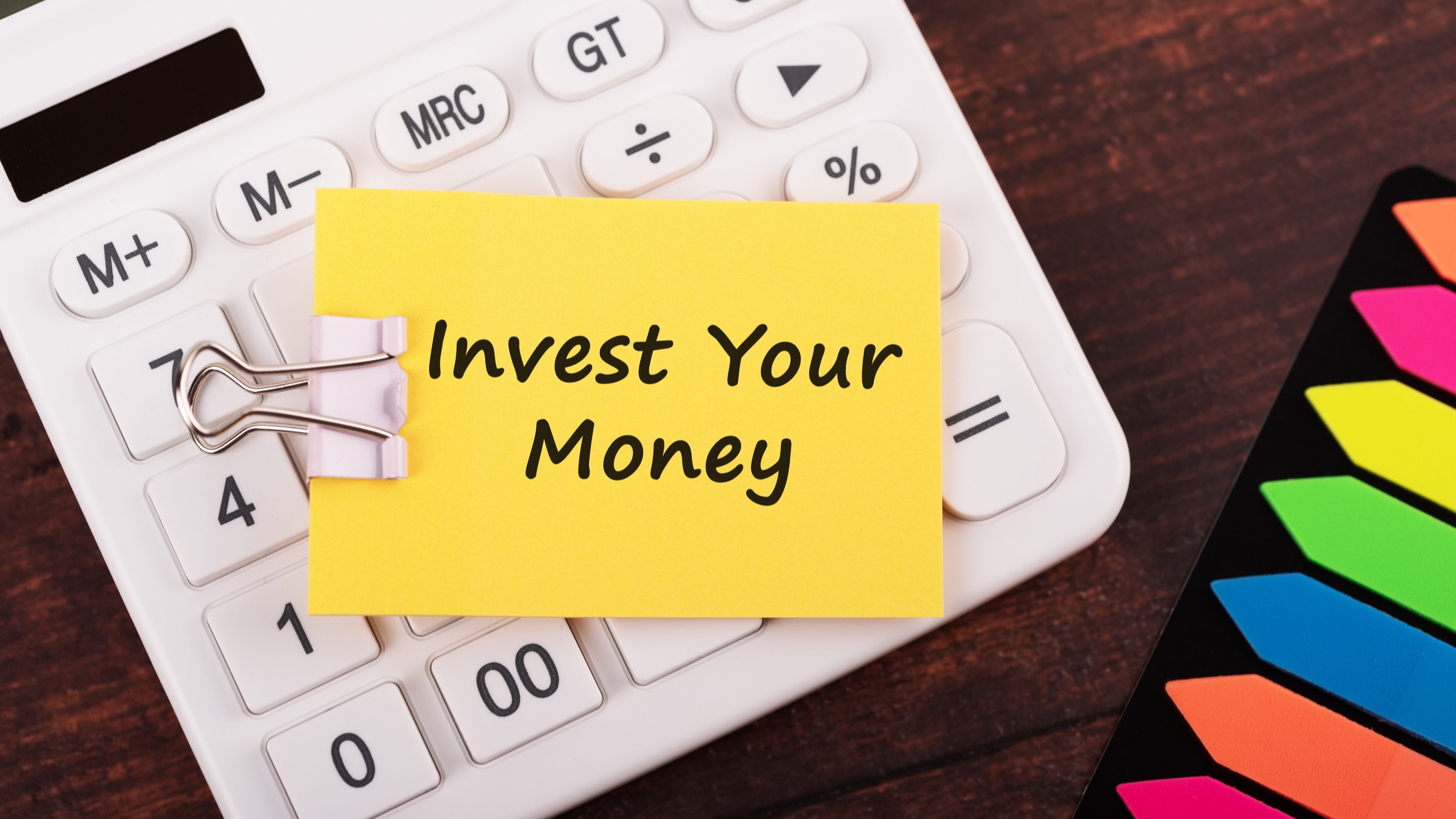 a yellow Post-it note placed on top of a calculator that reads "invest your money"