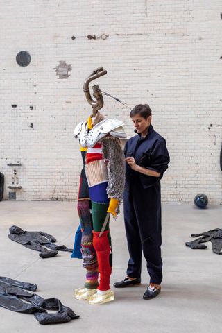 Alexandra Bircken with The Tourist, the central figure of her ‘Fair Game’ show at Kindl, Berlin. Sporting a motorcycle exhaust for a head, and carrying a sabre, she is clad in colourful attire, with epoxy resin clogs giving an illusion of levitation.