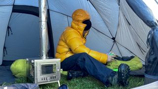 A man sits in a tent wearing a yellow The North Face Summit Series Pumori Down Parka.