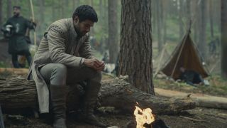 Ser Criston Cole looks sad as he sits by a fire in a forest in House of the Dragon's season 2 finale