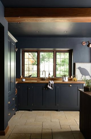 An all-black kitchen by deVOL with light stone flooring and bronze wall light