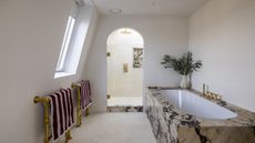 a simple bathroom decor showing a marble clad bath and an arched shower door into a neat pared back shower room