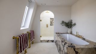 a simple bathroom decor showing a marble clad bath and an arched shower door into a neat pared back shower room