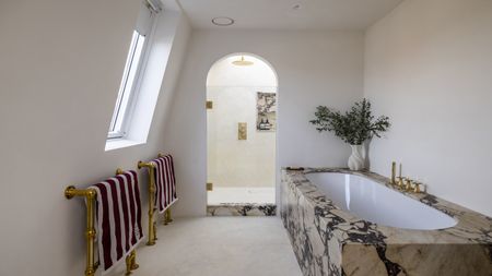 a simple bathroom decor showing a marble clad bath and an arched shower door into a neat pared back shower room