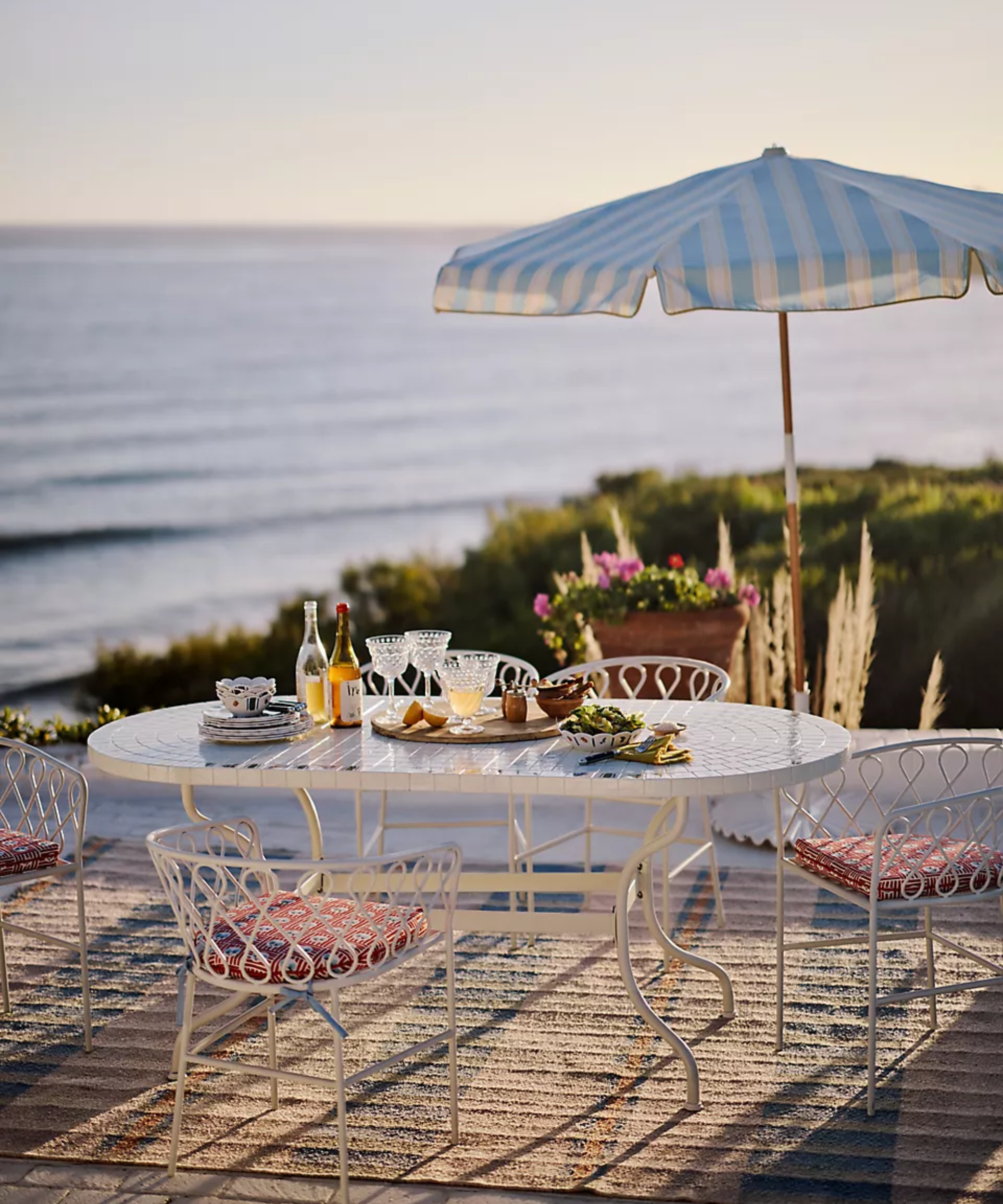 an outdoor dining set up with a white table, several chairs, and a blue striped umbrella