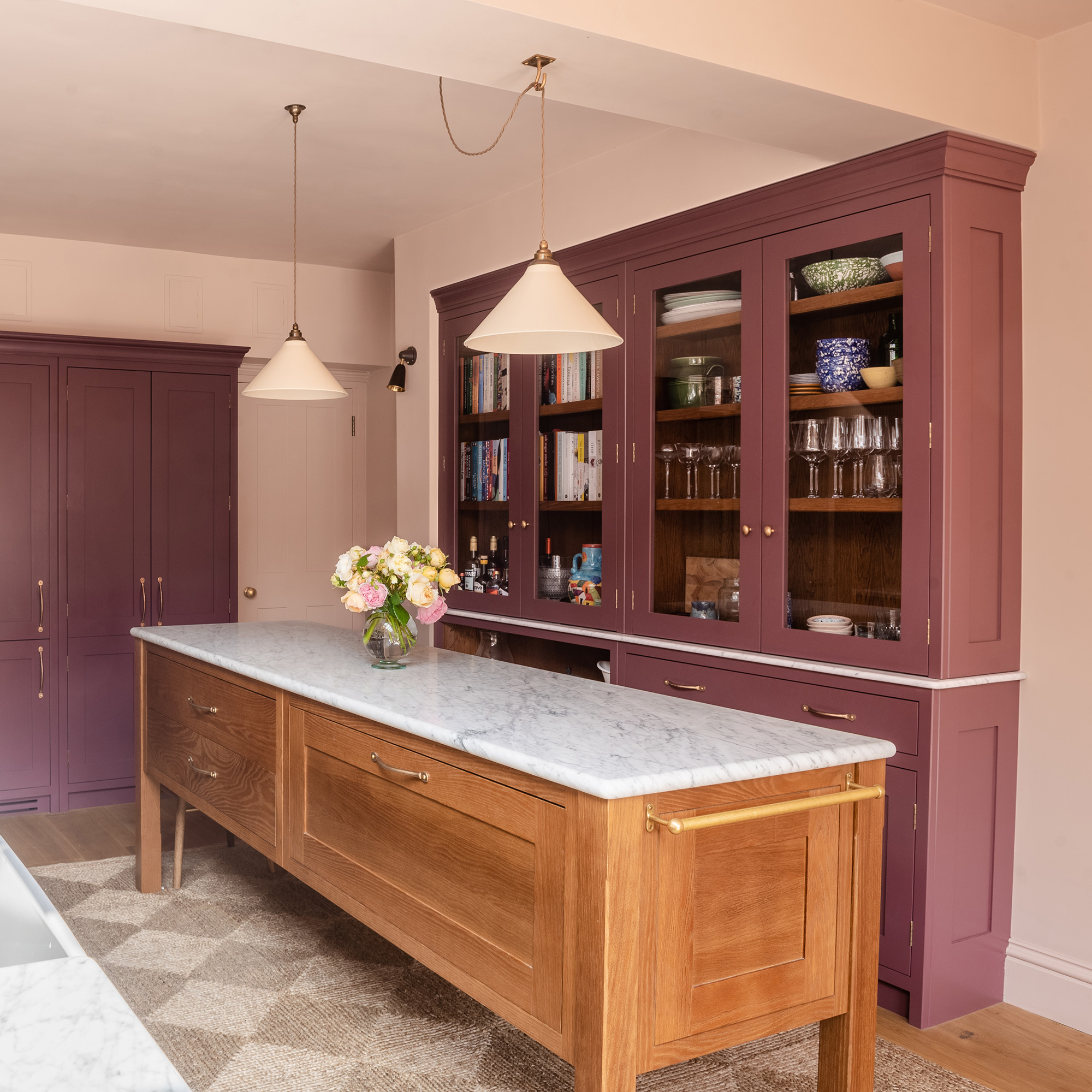 small kitchen with pink walls and purple cabinetry with wooden freestanding kitchen island and diamond patterned jute rug