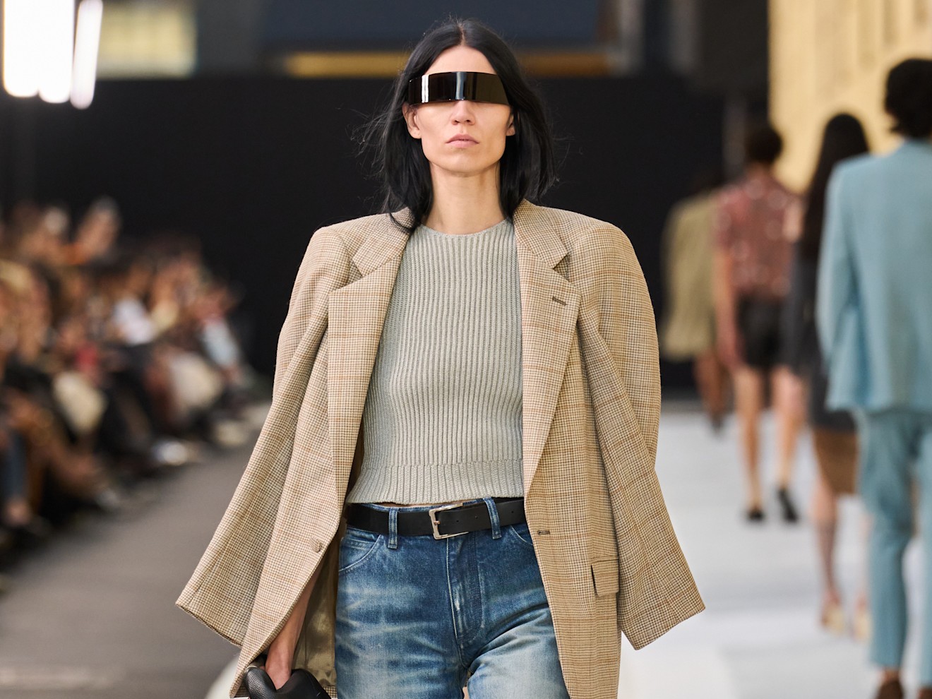 On the S/S 26 Margiela runway, a model wears washed out jeans, tan blazer, beige shirt, and a black belt.