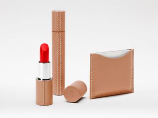 La Bouche rouge makeup collection in beige leather cases. An open case of red lipstick, a closed case of mascara and a card wallet against grey background