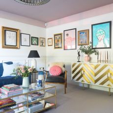 Living room with gallery wall, armchairs, gold chevron sideboard and glass coffee table