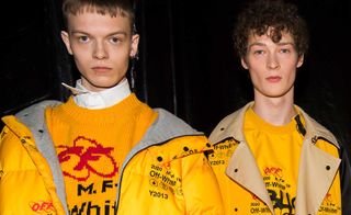 Two models looking directly at the lens wearing yellow coats and t shirts