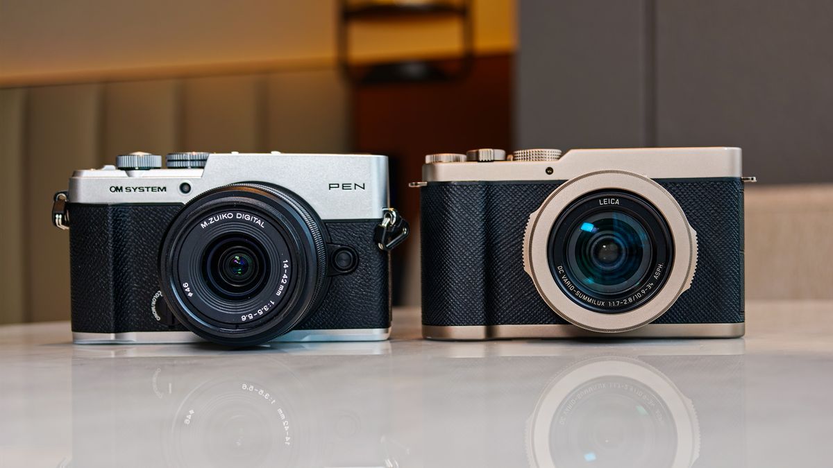 OM System PEN vs Panasonic Lumix L10: two micro four thirds cameras side by side on a white marble surface with lamp light in the background