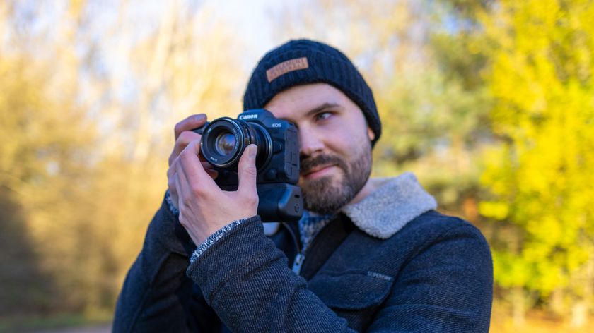 A picture of a photographer outside on a bright sunny day holding a Canon EOS R5 camera to his eye with a vintage Helios lens attached to it