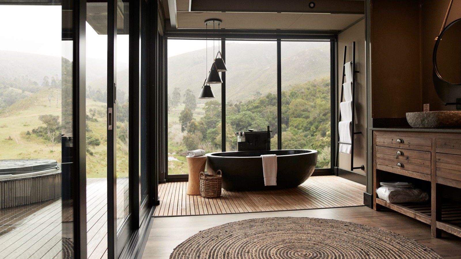 A black bathtub in a room with large windows and pendant lights hanging from the ceiling
