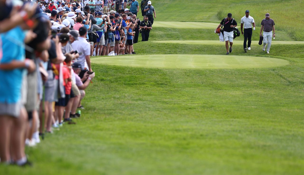 Tiger Woods walks down the fairway with fans either side